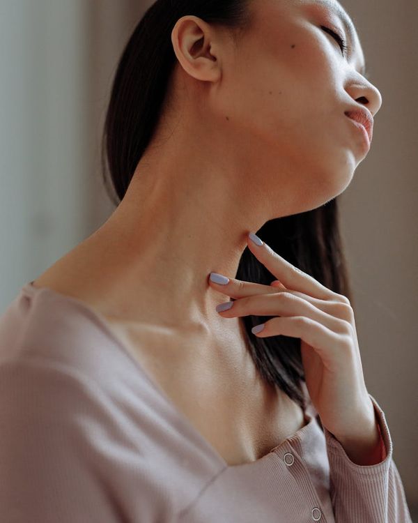 A serene woman with eyes closed, performing a gentle neck stretch in a softly lit room.